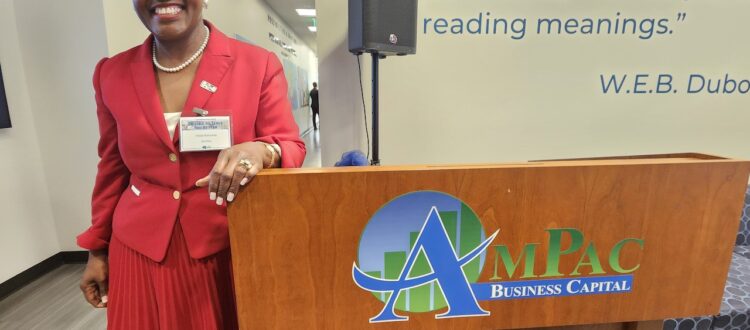 Hilda Kennedy, Founder and President of AmPac standing alongside the AmPac podium shortly after speaking to a room full of guests and supporters sharing key details of the merger and how excited she is to be able to boost the economic development in this region.
